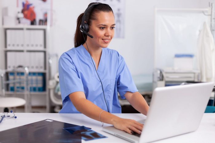 Photo of woman in scrubs in front of computer illustrates blog: "5 Reasons To Work With a Medical Billing Company"