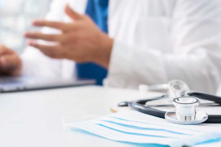 Photo of man in doctor's office with computer and stethoscope illustrates blog: "Med-Legal Billing Codes in California: a Quick Guide"
