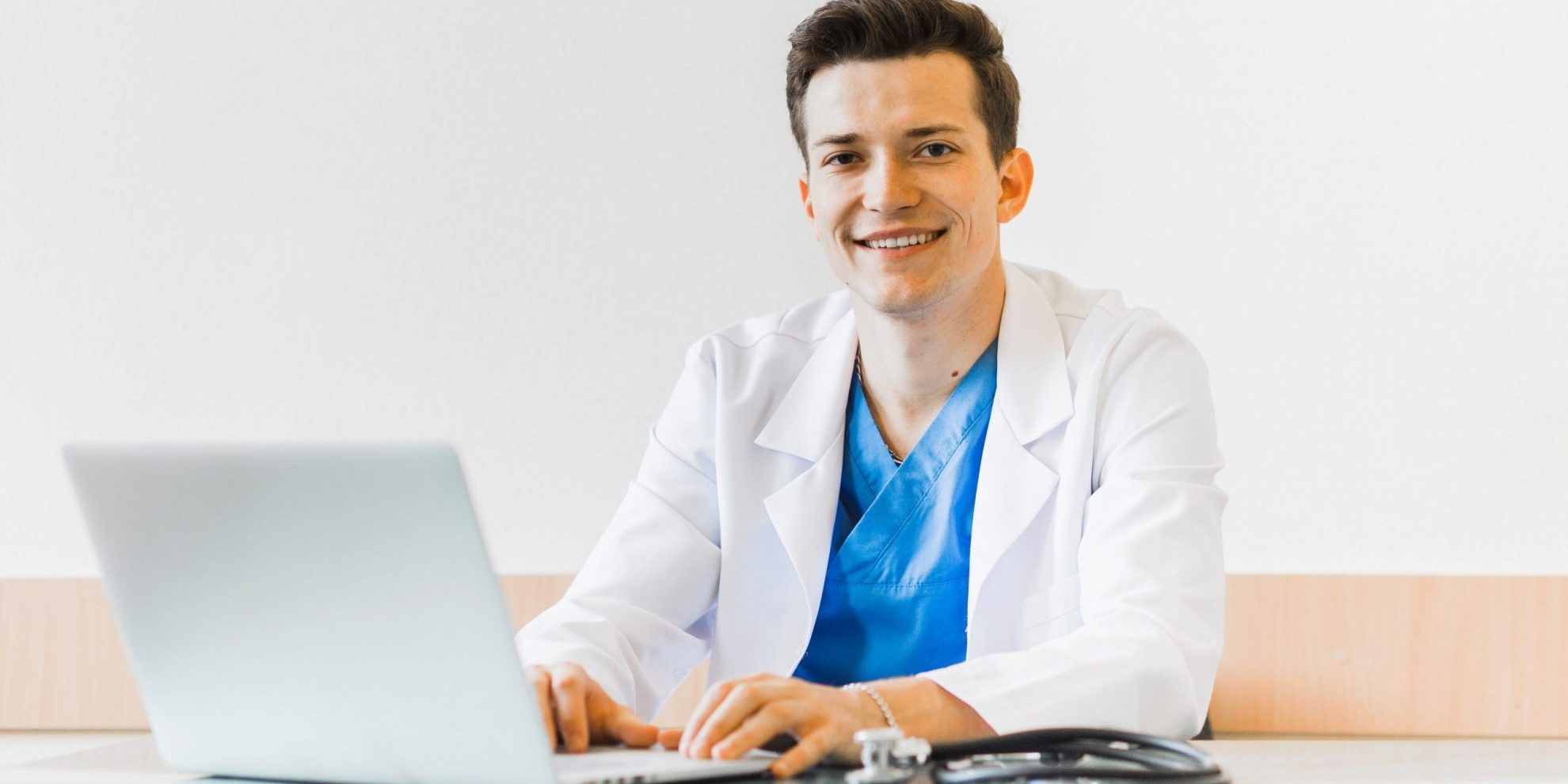 Photo of man in scrubs smiling in front of computer illustrates blog: "California Medical Legal Billing: What Is an EOR?