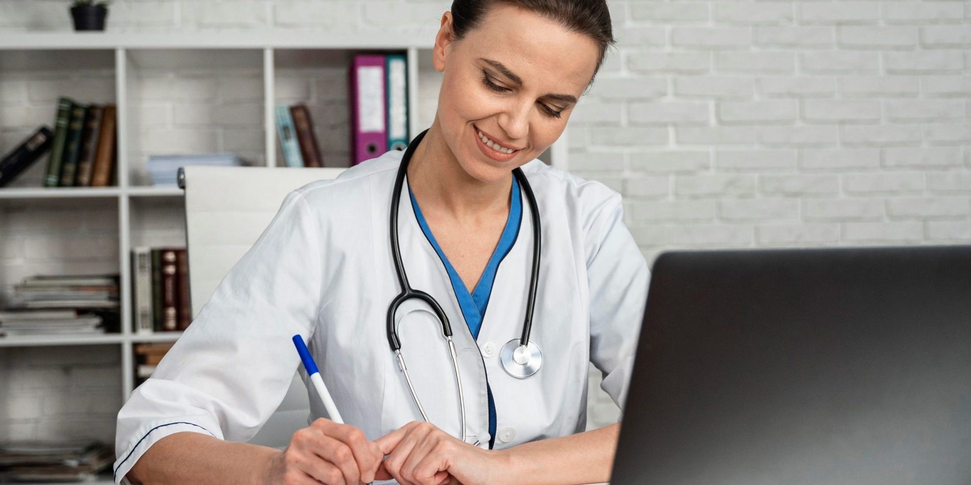 Female doctor writing in front of laptop illustrates blog "Can I Take the QME Examination Outside of California?"