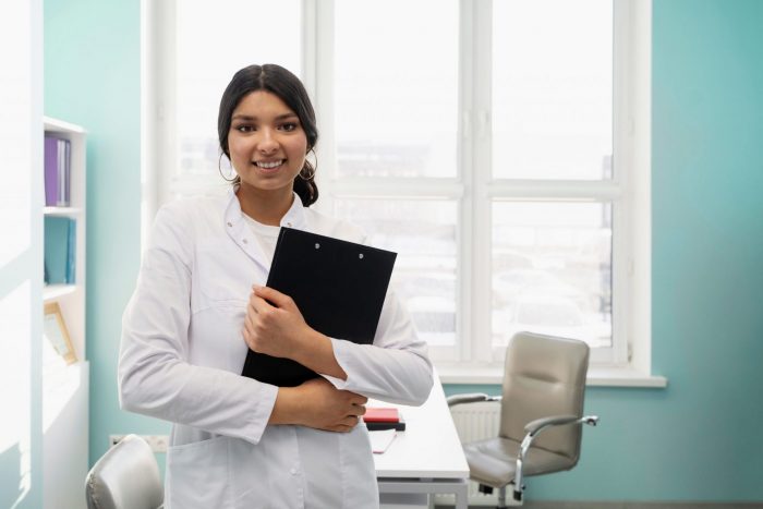 Female doctor holding clipboard illustrates blog "Is There a Fee To Be a QME in California?"