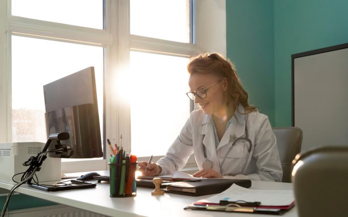 Female doctor sitting at desk in front of computer illustrates blog "Why Is Medical Billing Important?"