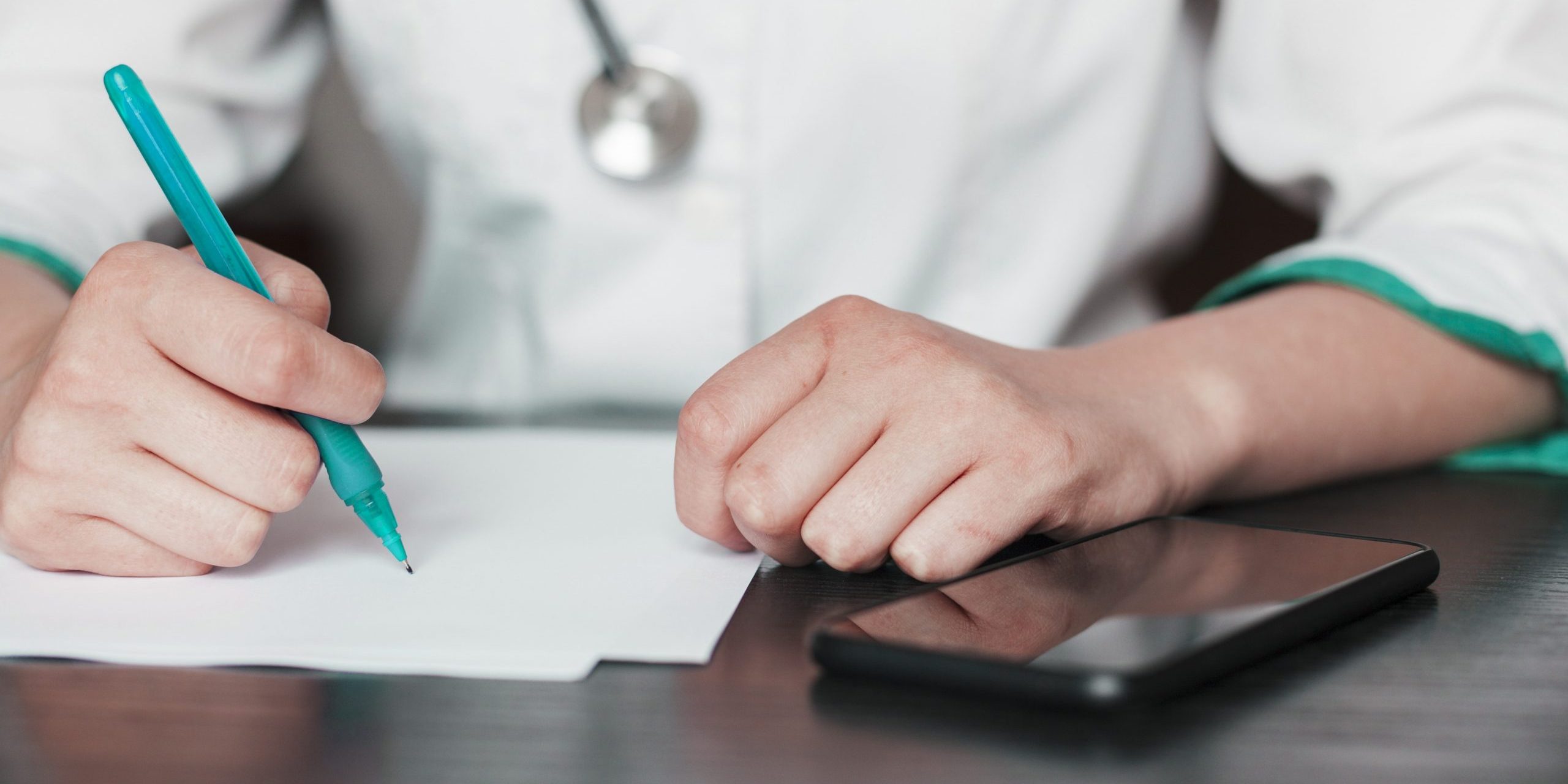 Closeup of woman in scrubs holding pen with calculator by her side illustrates blog "Medical Billing vs Medical Coding: What Is the Difference?"