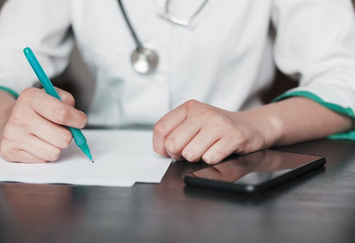 medical-billing2-fp Closeup of woman in scrubs holding pen with calculator by her side illustrates blog "Medical Billing vs Medical Coding: What Is the Difference?"