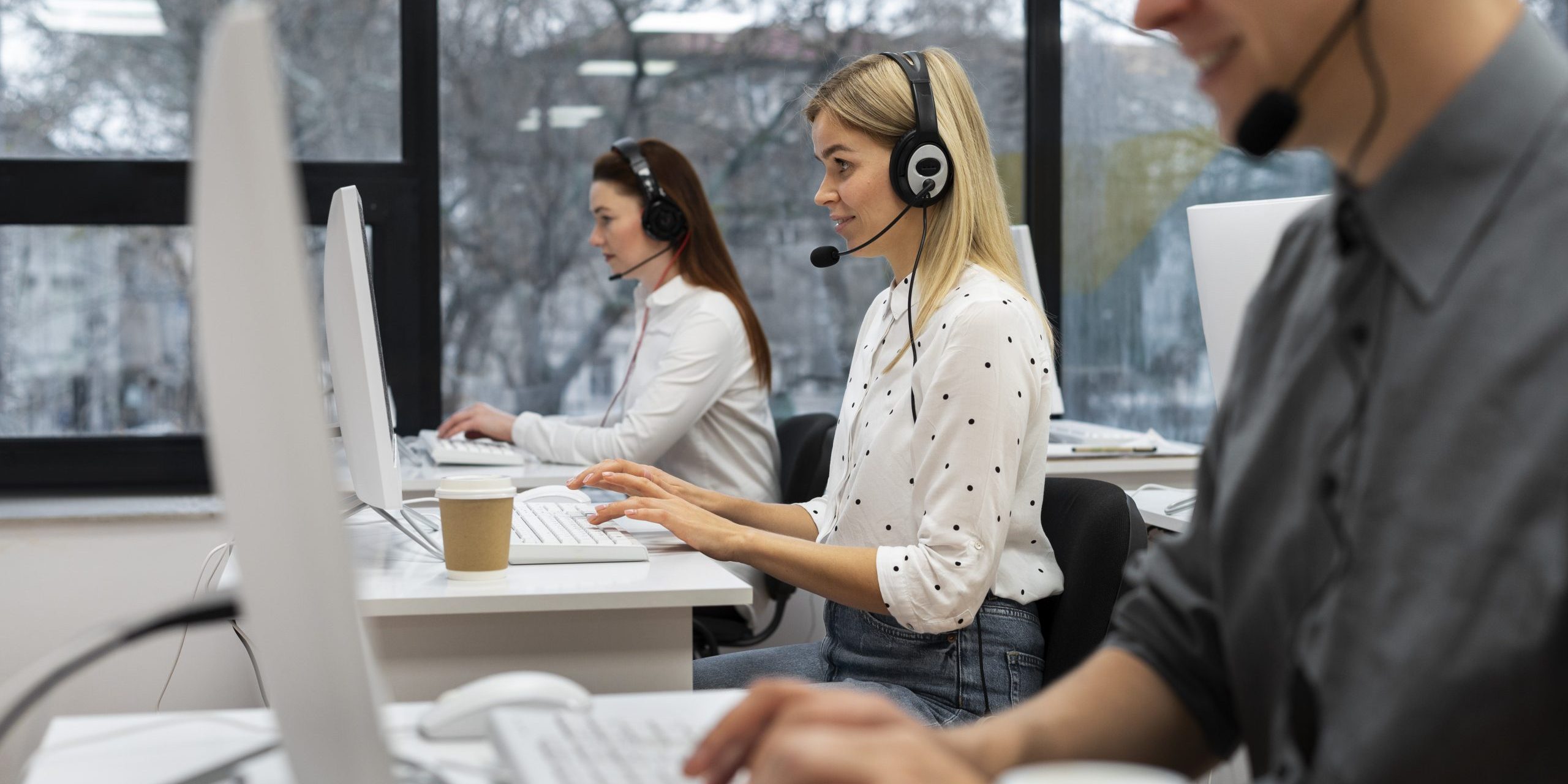 calls-fp Three people sitting at desks in call center.