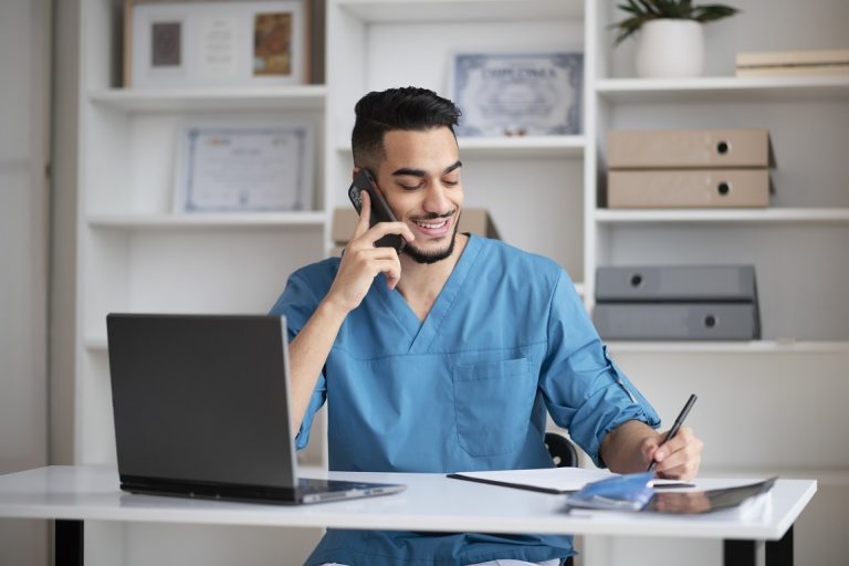 Man in scrubs talking on phone illustrates blog "Benefits of an Efficient Healthcare Call Center"