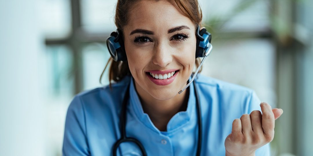 Happy female doctor working at medical call center. Woman in scrubs and call center headset illustrates blog "Enhancing Patient Experience Through Healthcare Call Center Innovations"