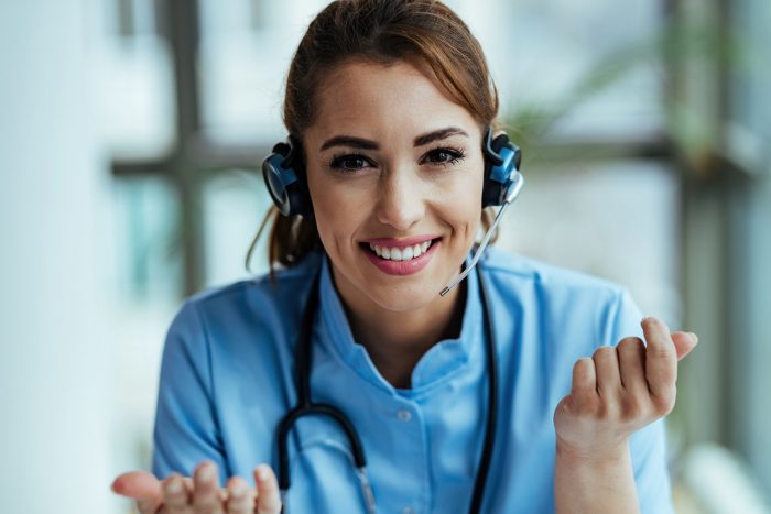 Happy female doctor working at medical call center. Woman in scrubs and call center headset illustrates blog "Enhancing Patient Experience Through Healthcare Call Center Innovations"