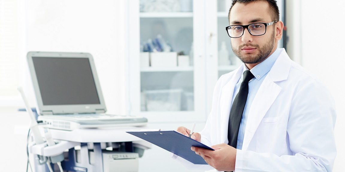 Male doctor holding clipboard illustrates blog "What Is Healthcare Management?"