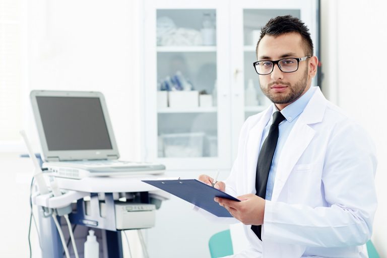 Male doctor holding clipboard illustrates blog "What Is Healthcare Management?"